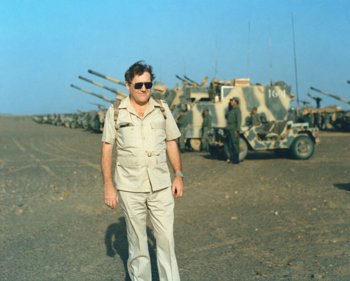 Colin McGregor in front of artillery vehicles in the desert